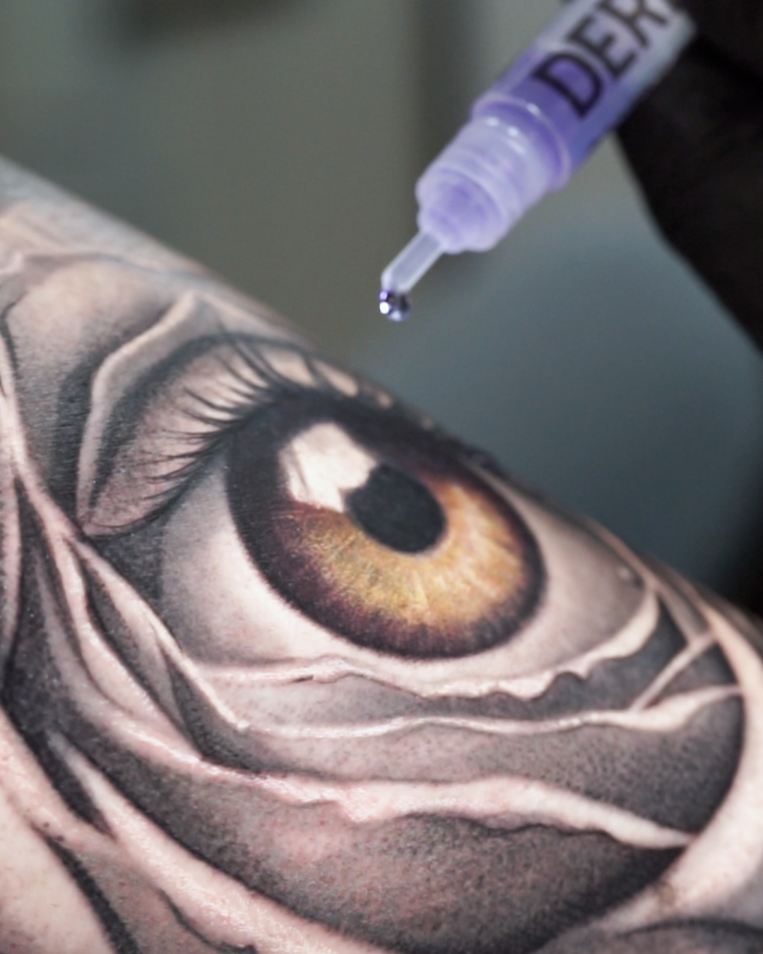 DERM·X Stick applying protective adhesive over a fresh realistic eye tattoo